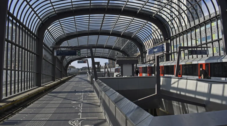 Metro train and sunlit platforms beneath the glass canopy of Noord station in Amsterdam