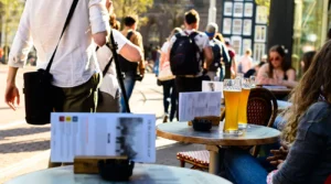 Outdoor caf&eacute; in Amsterdam with glasses of beer on a terrace and tourists walking along the street