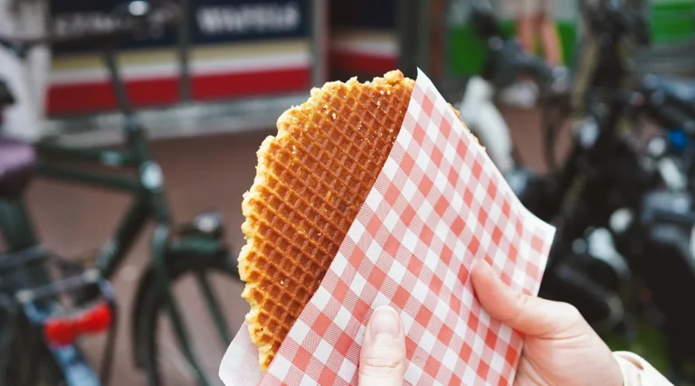 Traditional Dutch stroopwafel held in hand on an Amsterdam street with bicycles in the background