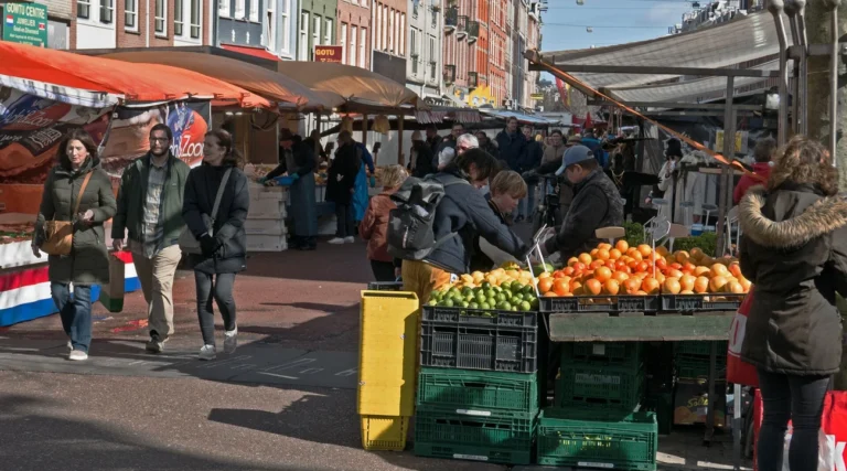 Sunlit fruit stall and shoppers at Albert Cuyp market in Amsterdam De Pijp, March 2023