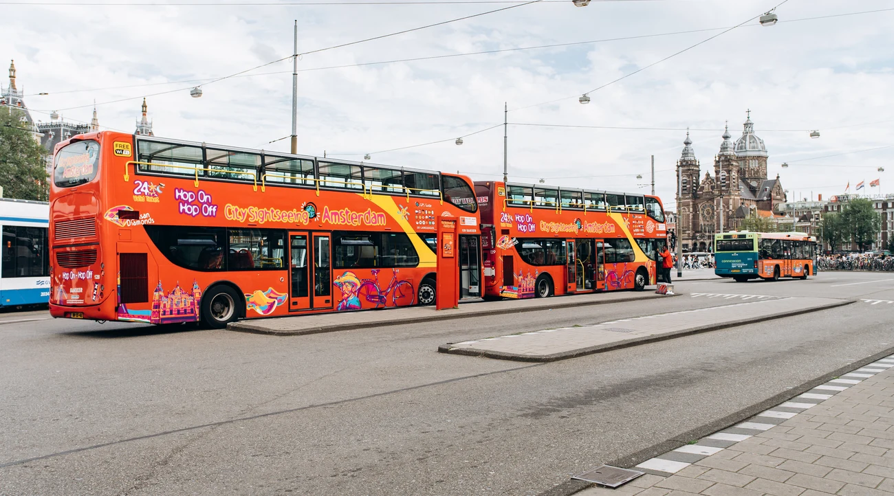 Red City Sightseeing hop-on hop-off buses near Amsterdam Central Station in daylight