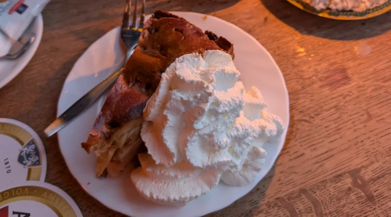 Homemade apple pie with whipped cream on a wooden caf&eacute; table at Caf&eacute; &rsquo;t Papeneiland in Amsterdam&rsquo;s Jordaan