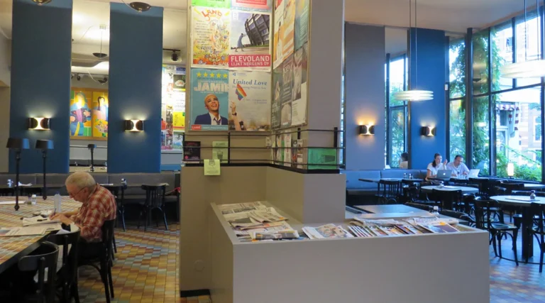 Bright interior, reading table and poster-covered central pillar at Caf&eacute; de Jaren in Amsterdam, photographed in July 2019