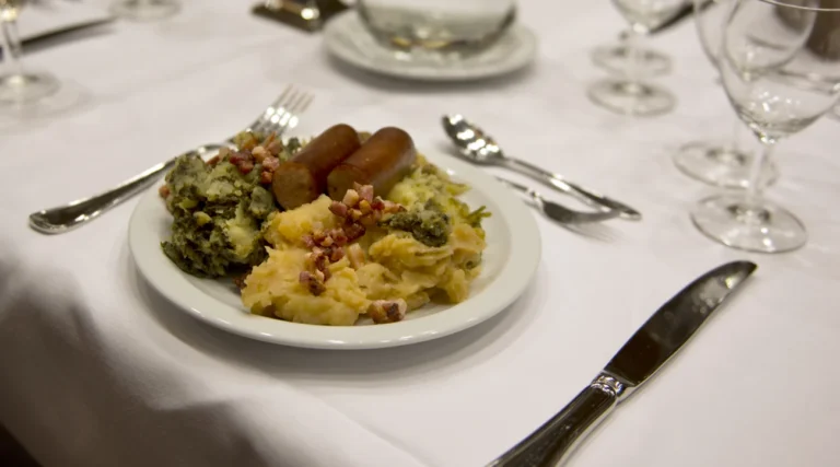 Dutch stamppot made with mashed potatoes and vegetables, served with sausages and bacon on a restaurant table