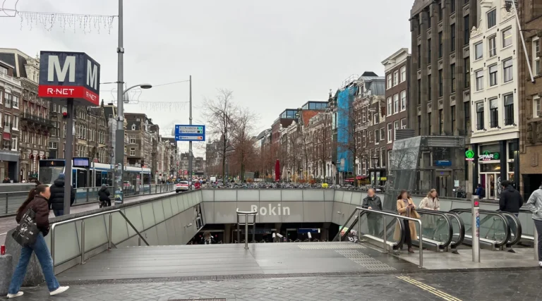 Entrance and escalators of Rokin metro station beside trams and historic buildings in central Amsterdam