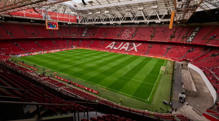 Football pitch, red Ajax stands and roof structure inside Johan Cruijff ArenA in Amsterdam