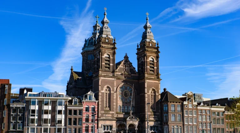 Twin towers and dome of Saint Nicholas Basilica opposite Amsterdam Centraal under a blue daytime sky