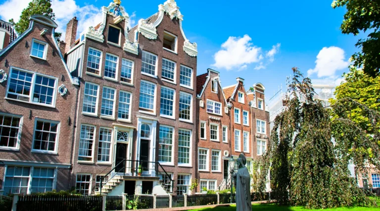 Gabled historic houses, green lawn and a beguine statue in Amsterdam&rsquo;s Begijnhof courtyard in daylight