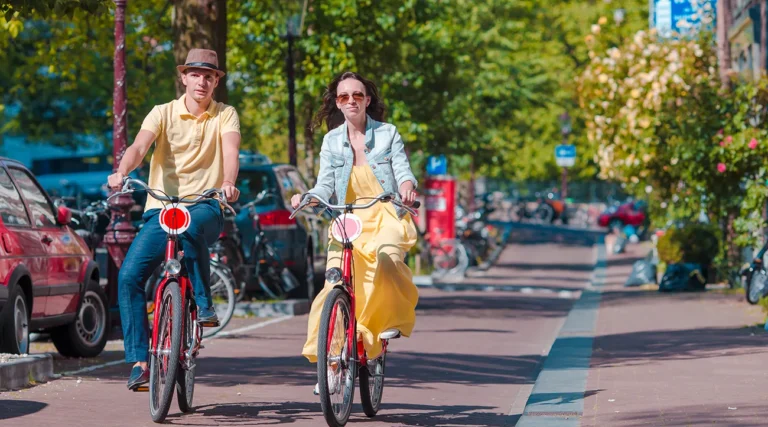 Couple riding bicycles along a tree-lined city street on a sunny day