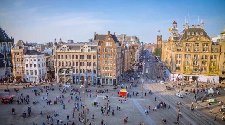 Dam Square and Damrak in Amsterdam in daylight, with historic buildings and pedestrians