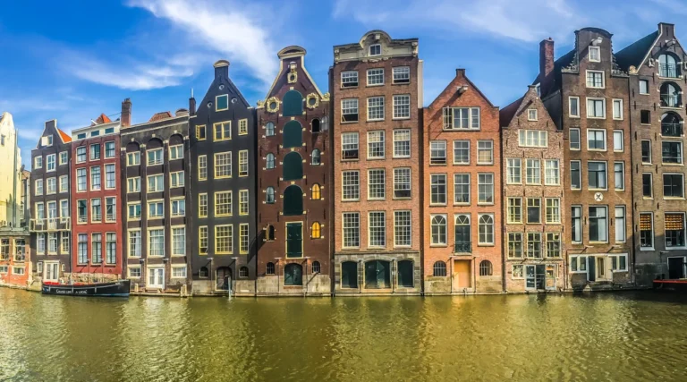 Gabled houses reflected in the Damrak waterfront in Amsterdam on a sunny day