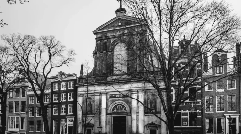 Daylight black-and-white view of De Duif church facade among canal houses and trees on Prinsengracht in Amsterdam