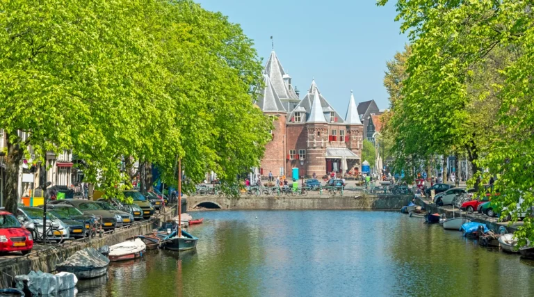 De Waag in Amsterdam seen along the tree-lined Kloveniersburgwal canal on a sunny day