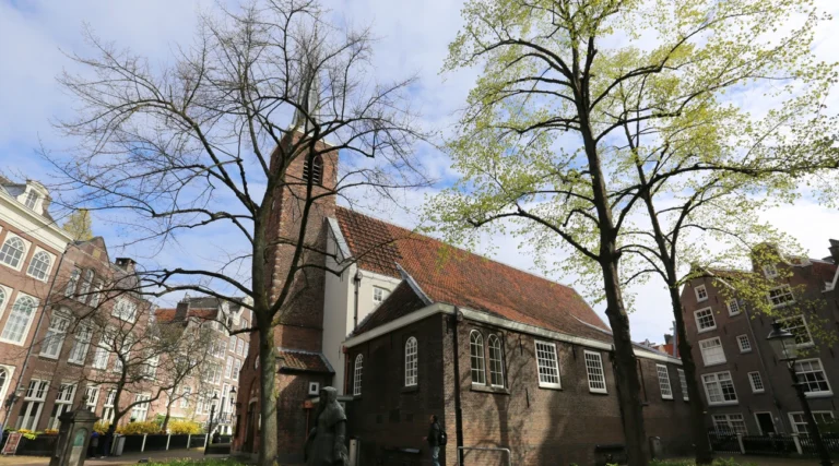English Reformed Church with its brick tower and tiled roof among trees in Amsterdam&rsquo;s Begijnhof in daylight