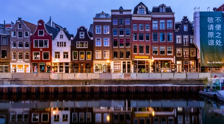 A picturesque view of colorful canal houses reflecting on the water in Amsterdam, Netherlands.