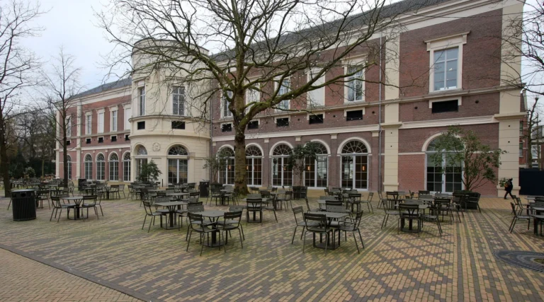 Historic Groote Museum building beside the trees and tables of Artisplein in Amsterdam