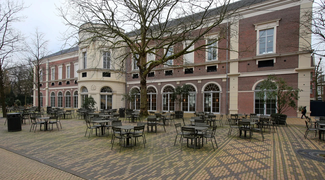 Historic Groote Museum building beside the trees and tables of Artisplein in Amsterdam