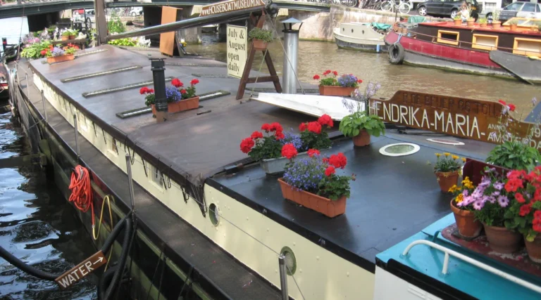 Flower-covered roof and name sign of the Hendrika Maria Houseboat Museum moored on Prinsengracht in Amsterdam in daylight