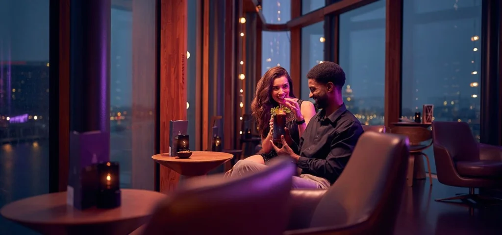 Guests enjoying cocktails beside panoramic windows at Malabar sky bar in Hotel Jakarta, Amsterdam