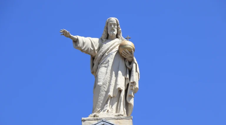 White statue of Christ on the roof of Moses and Aaron Church in Amsterdam against a blue daytime sky