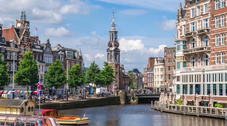 Munttoren clock tower beside the Amstel in Amsterdam on a bright day, with boats and historic canal buildings