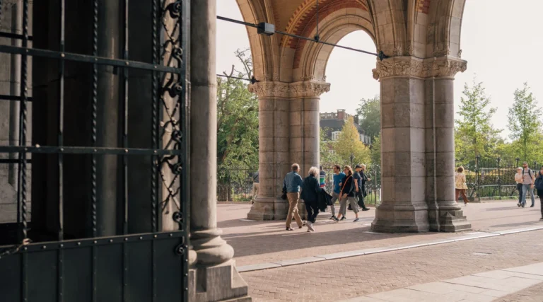 People walk under arches at Amsterdam's iconic Rijksmuseum, showcasing its architectural beauty.