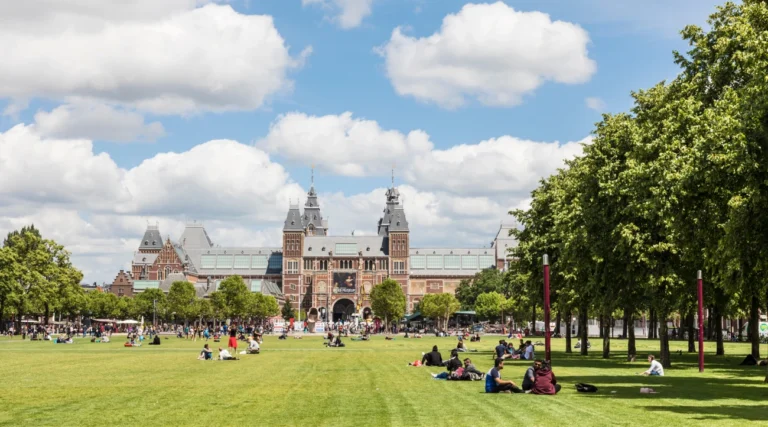 People relaxing on the green lawns of Museumplein with the Rijksmuseum in the background on a sunny day
