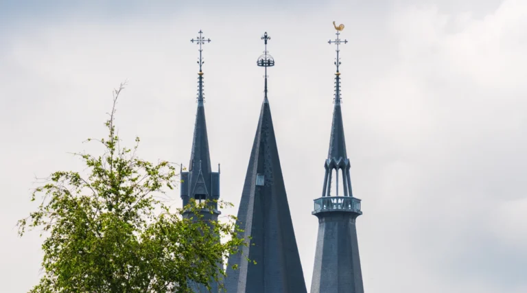 Three slender spires of the Posthoornkerk rising above green trees in Amsterdam in daylight