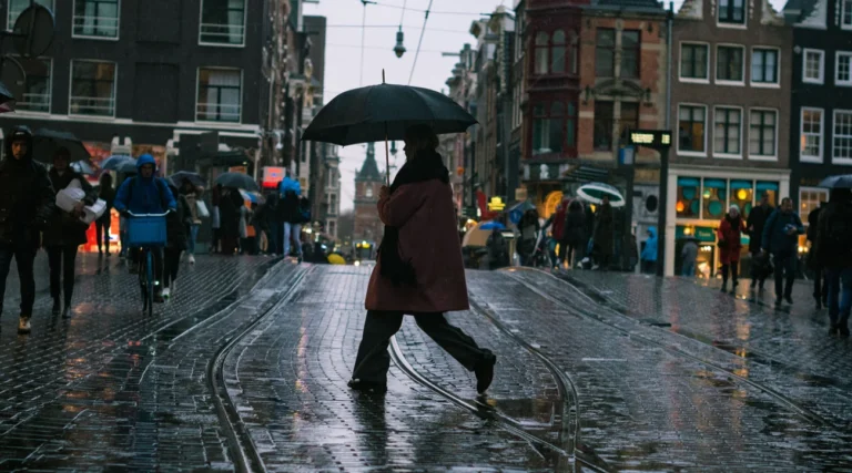 A person walks with an umbrella on a rainy day in Amsterdam's historic streets.