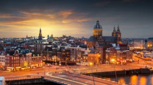 Amsterdam skyline at sunset, with the Basilica of Saint Nicholas and illuminated buildings beside the water
