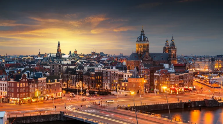 Amsterdam skyline at sunset, with the Basilica of Saint Nicholas and illuminated buildings beside the water