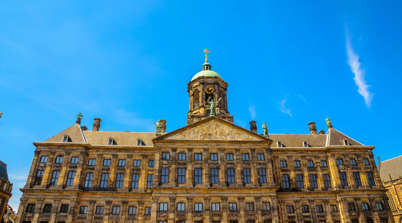 Royal Palace Amsterdam facade and clock tower on Dam Square beneath a blue daytime sky