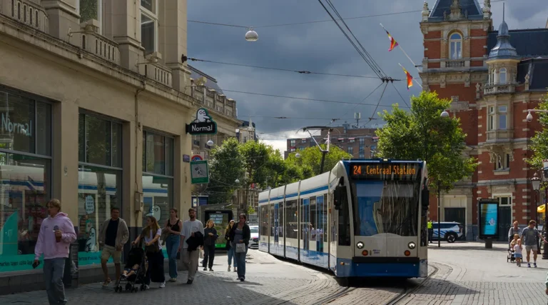 People walking side of a tram, historical building backdrop.