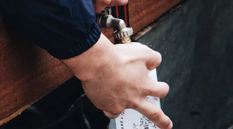 Close-up of hands refilling a water bottle from an outdoor faucet, emphasizing hydration and sustainability.