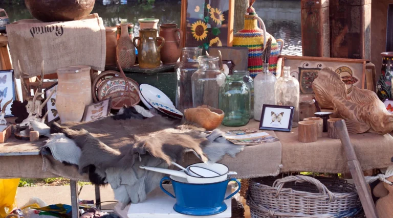 Second-hand pottery, glass jars, baskets and an enamel pot on a sunlit stall at Waterlooplein flea market in Amsterdam