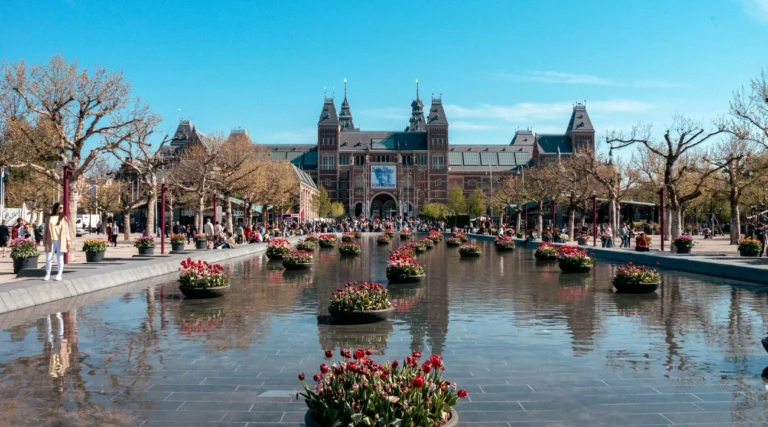 Rijksmuseum view in Amsterdam with tulip planters and a reflective pond, highlighting its iconic architecture.
