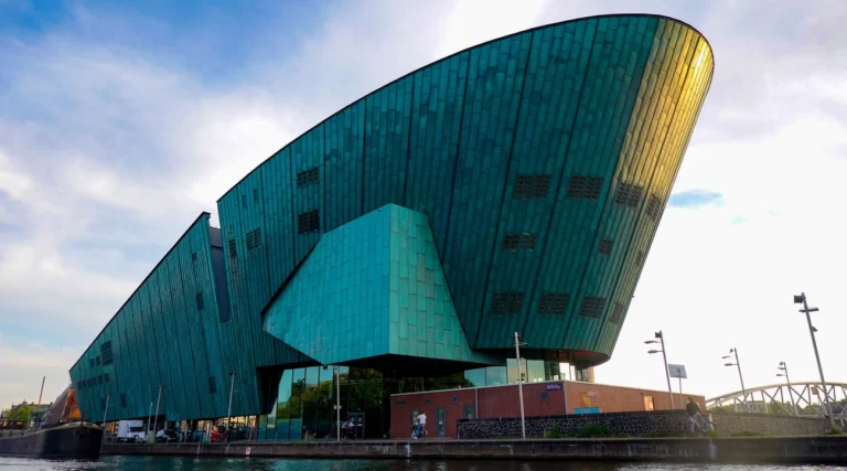 The NEMO Science Museum in Amsterdam with its iconic modern architecture beside a tranquil river.